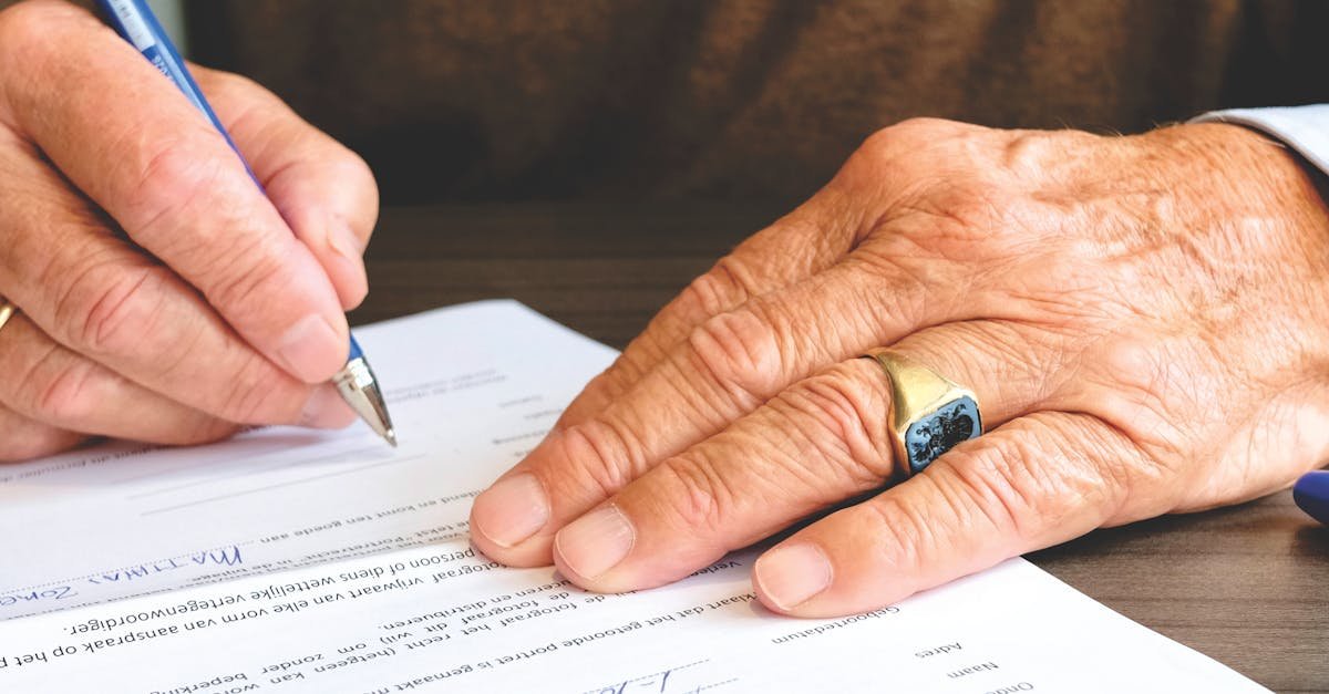 Close-up of a senior adult signing a legal document with a focus on hand and gold ring.